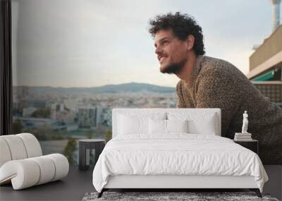 Guy looks at the city from the balcony, enjoys the beautiful view Wall mural