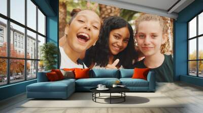 Three girls friends pre-teenage standing on the street smiling, hugging each other making faces for the camera. Three teenagers on the outdoors in urban cityscape background Wall mural