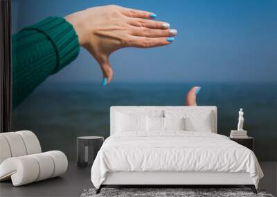 Close-up point of view shot photography of female caucasian hands isolated on blue sky background. Young woman forming frame with her two hands as if looking at something virtual and invisible Wall mural