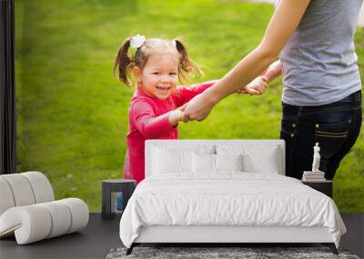 Closeup portrait of happy family holding hands while spinning around together. Little funny girl of 4 years age plays outside with her mother in spring city park. Horizontal color photography. Wall mural