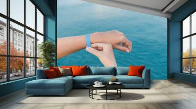 Closeup view of two white hands of woman isolated at blue blurry sea water background. Blue rubber wristband at wrist of one female hand. Horizontal color photography. Wall mural