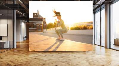 Sporty woman doing jumping squats exercises on stairs in park. Bodyweight training on sunset. Wall mural