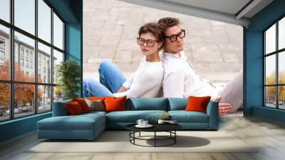 two attractive students man and woman wearing stylish glasses sitting floor Wall mural