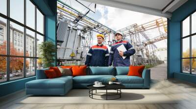 Two specialist electrical substation engineers inspect modern high-voltage equipment in the evening. Energy. Industry Wall mural