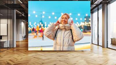 Woman winter Christmas modd Lovely middle-aged female warm winter jackets fur headphones stands ice rink background Town Square lifestyle Happy holiday woman walk snowy day Winter leisure Wall mural