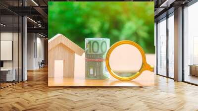 Euro banknotes and magnifying glass stand near a wooden house. Real estate concept. Search for affordable housing. Rent an apartment at a reasonable price. Mortgage and loan. Investment in building Wall mural