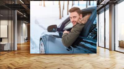 Young attractive Caucasian man sits at the wheel of his car sunny winter day. Wall mural