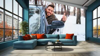 Young attractive Caucasian man sits at the wheel of his car sunny winter day. Wall mural