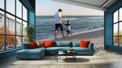 Young Caucasian dad with little son walk warm summer day along the sea coast. Summer family vacation concept. Friendship father and son. Happy childhood on the beach with parent. free space for text Wall mural