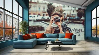 Young female tourist visiting old town on vacation and taking photos on old camera on the street. Wall mural