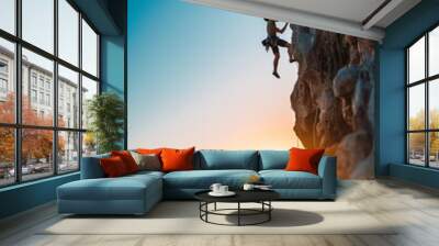 A climber, silhouetted against the sunset, scales a cliff, exemplifying freedom and extreme sport. Wall mural