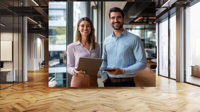 A man and a woman are standing in a room with a laptop and a tablet. They are smiling and seem to be happy Wall mural