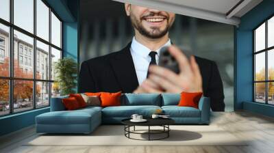 A man in a suit is smiling while looking at his cell phone. He is wearing a tie and he is in a professional setting Wall mural