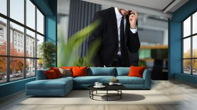 A man in a suit is talking on his cell phone while writing with a pencil. He is in a professional setting, possibly at work or in a business meeting. Concept of focus and productivity Wall mural