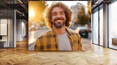 A man with a plaid shirt and curly hair is smiling in front of a car. Concept of happiness and contentment Wall mural