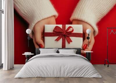 A person is holding a white gift box with a red ribbon. Concept of joy and excitement, as the person is likely presenting the gift to someone special. The red ribbon adds a festive touch to the scene Wall mural