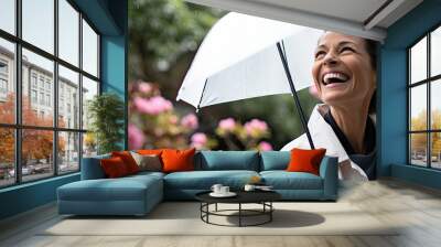 A relaxed, mature woman with an umbrella enjoys nature in a blooming garden during summer. Wall mural