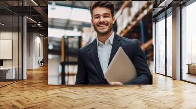 A smiling businessman in a suit manages warehouse operations, overseeing shipping and distribution with a laptop. Wall mural