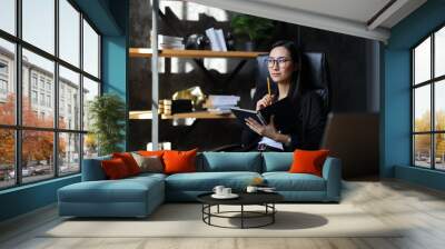 A successful young Asian businesswoman in her office, thinking and working on her computer. Wall mural