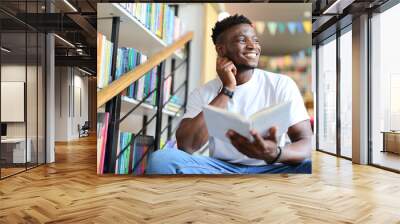 A young man engrossed in studying at a library, surrounded by books and knowledge. Wall mural