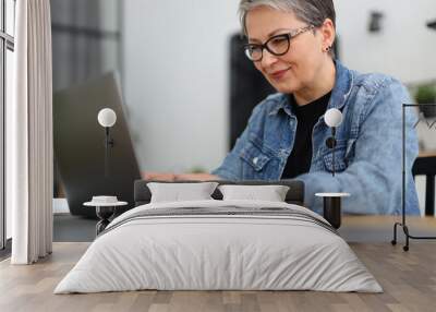 Busy senior smiling woman at workplace with laptop. Wall mural