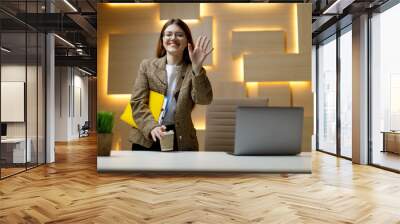 First day at the office. A young girl smiles and shows a gesture of welcome at the workplace. Wall mural