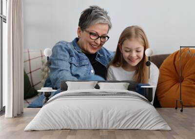 Happy grandmother and granddaughter watching fun content on phone in home interior. Wall mural