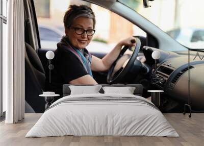 Happy senior woman in glasses driving her own car. Wall mural