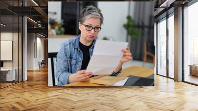 Upset senior woman reading mail or bill at table. Wall mural