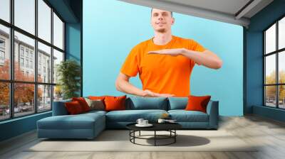 A young man holding an object with both hands in front of him, showing, offering, or advertising an object against a blue wall. Empty. Space. Concept. Object. Background. Portrait. Young. Copy Wall mural