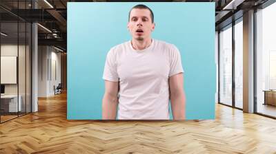 An unmotivated exhausted young man in a white t-shirt with open mouth on a blue background. Arm. Mid Adult. Boring. Bad. Boredom. Boy. Disturb. Lazy. Work. Goatee. Stare. Stress. Upset. Woke up Wall mural