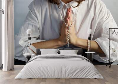 A young woman, in a white shirt folding a lodon to each other prays to God holding rosary.  Wall mural