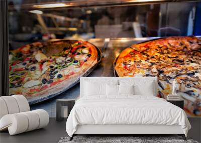 Closeup of fresh large crust pizzas in store cafe on display restaurant in Italy with melted mozzarella cheese and olive vegetables tomato sauce slices Wall mural