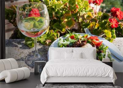 Closeup of one glass of white in garden with red geranium flowers outside in Tuscany Italy summer and salad Wall mural