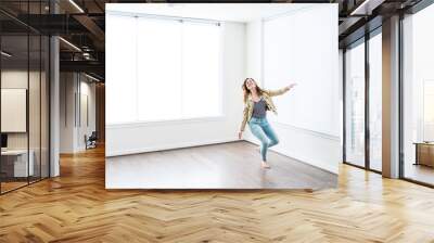 One young happy smiling woman jumping up in empty modern new room with hardwood floors and large sunny windows in apartment Wall mural