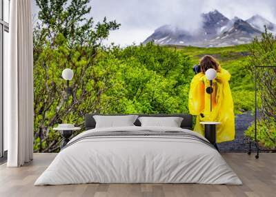 Skaftafell, Iceland green summer lush landscape view of woman tourist in yellow poncho walking hiking on wet trail path hiking road rainy day in mountains Wall mural