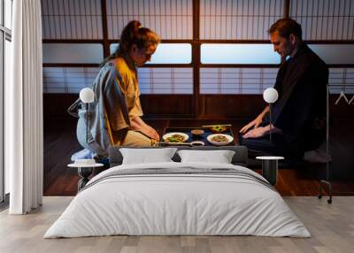 Young couple seiza sitting on hardwood floor pillows at traditional Japanese in ryokan kaiseki dishes of soba noodles, natto, edamame and soy sauce on table by shoji sliding paper doors Wall mural