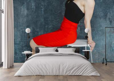 Fashion portrait of a stylish brunette girl wearing a black dress. Woman with long hair wearing red earrings. Model sitting on chair. Set on a gray background Wall mural