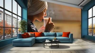 Banner of young beautiful woman is drinking hot steaming coffee or tea in sunshine light on balcony in hotel or home. Fresh girl after shower wearing in towel on head relaxing in the morning. Wall mural