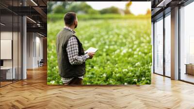 Farmer or agronomist uses digital tablet to analyse and check the growth and disease of the blooming plants in the potato field. Smart farming technology and agriculture business concept. Wall mural