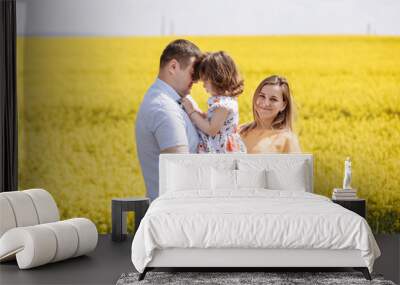 Happy pregnant family with little daughter spending time together in a yellow rapeseed field on summer day Wall mural