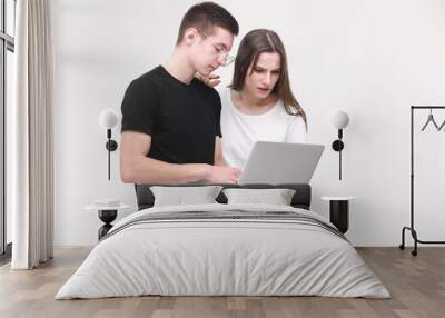 Two serious teenager guy and girl are using laptop and discussing something on white background in studio. Male and female surprised Wall mural