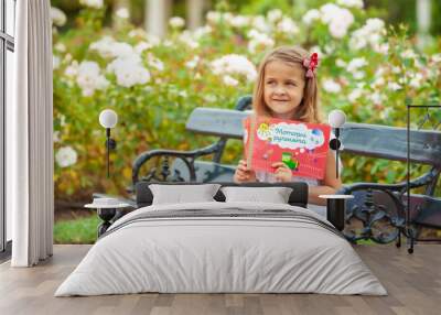 little girl with a book in her hands in the park outdoors Wall mural