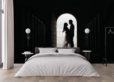 Silhouette of loving couple hugging while standing in doorway on black background, Bride and groom in wedding day posing in a doorway Wall mural