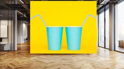 Two blue paper cups with drinking colored plastic straws on yellow background. Set for party. Minimalist Style. Copy, empty space for text Wall mural