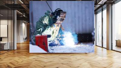 Welder in protective clothing and special protective mask performs welding work in winter. Wall mural