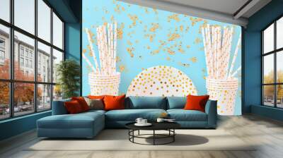 Birthday or party paper glasses with straws, dish and golden sequins on blue background. Wall mural