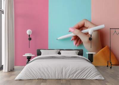 Close-up of a female hand with pink nails holding a pen on a colorful pastel background. Wall mural