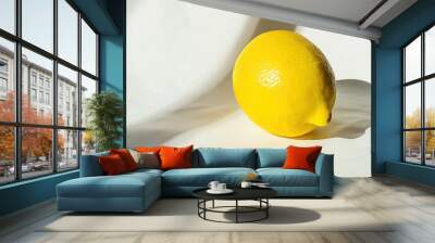 Close-up of a vibrant yellow lemon on a white surface, casting a subtle shadow. Wall mural