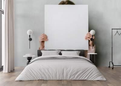 Person holding a blank white board, obscuring their face against a neutral background. Wall mural